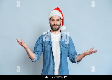 Freundlicher, lächelnder kaukasischer Mann mit Weihnachtsmütze, der die Begrüßung über der Wand gestikuliert Stockfoto