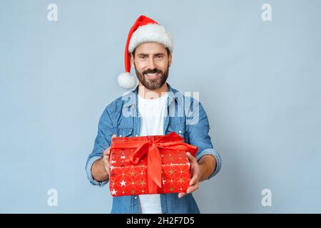 Porträt eines lächelnden Mannes in Santa Hut geben Geschenkbox auf blauem Hintergrund Stockfoto
