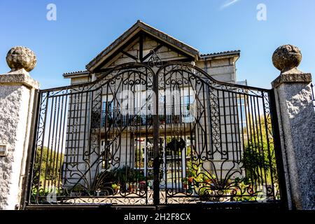 Schmiedeeiserne Tür, die ein graues Steinhaus mit Pflanzen auf dem Balkon und im unteren Teil hält Stockfoto