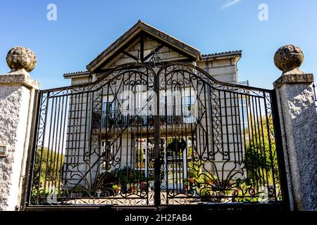 Schmiedeeiserne Tür, die ein graues Steinhaus mit Pflanzen auf dem Balkon und im unteren Teil hält Stockfoto