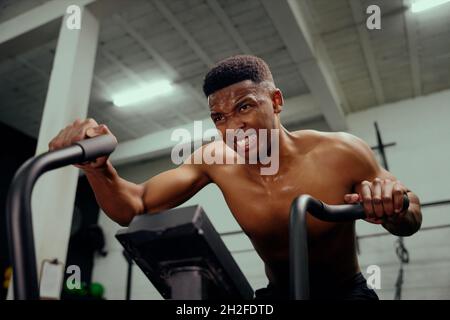 Afroamerikanischer Mann mit einem Ellipsentrainer, der intensives Training macht. Männlicher Athlet, der intensiv im Fitnessstudio trainiert. Hochwertige Fotos Stockfoto