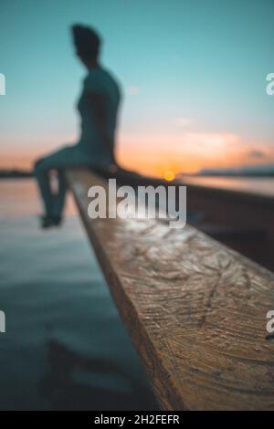 Schöne Frau sitzt am Ende des Bootes auf dem Fluss während eines surrealen Sonnenuntergangs Stockfoto