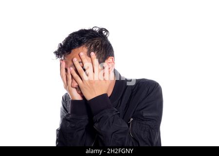 Peinlicher Mann, der sein Gesicht mit den Händen bedeckt. Weißer Hintergrund. Mann bedeckt sein Gesicht und blickt mit den Fingern auf die Kamera. Stockfoto