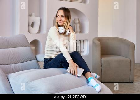 Sofa in der Lounge mit einer Frau in Kopfhörern, die darauf sitzt. Stockfoto
