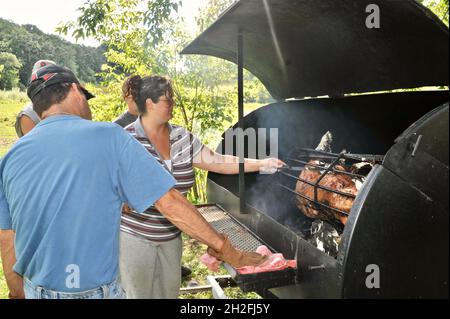 Zubereitung und Spieß-Rösten von ganzen Schwein draußen auf einem Grill, über Holzkohle, auf einer Farm im Mittleren Westen, Blanchardville, Wisconsin, USA Stockfoto