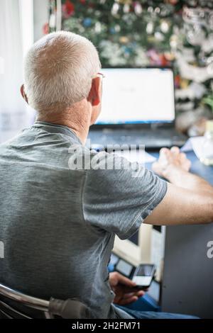 Ein älterer Mann mit kahlem Kopf arbeitet auf dem Laptop. Der alte Mann drehte sich um und setzte sich auf einen Stuhl. Stockfoto