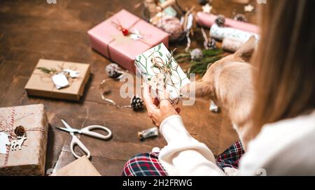 Frau mit Hund Verpackung Weihnachten Geschenkboxen, Nahaufnahme. 3/4-Frauen sitzen und bereiten natürliche Öko-Geschenke auf dem Boden mit Dekorelementen zu Stockfoto