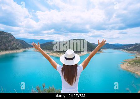 Frau Tourist in Sonnenhut mit offenen Armen genießen die Natur und tolle Aussicht auf den See mit reinem blauem Wasser. Gutes Leben, Freiheit Stockfoto