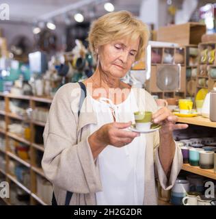 Reife weibliche Käufer wählt Tassen für Tee oder Kaffee im Geschirrladen Stockfoto