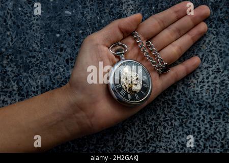 Eine Retro-Taschenuhr mit Kette in der Handfläche des Mädchens. Wandhintergrund. Stockfoto