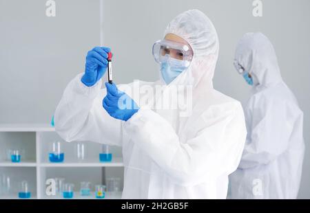 Epidemiologische Forscher in Virusschutzkleidung untersuchen Blutproben von Patienten in einem Reagenzglas mit Schraubverschluss. Coronavirus-Krankheit 2019 (C Stockfoto