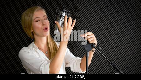 Junge kaukasische Frau singt vor schwarzen Schallschutzwänden. Musiker, die Musik im professionellen Aufnahmestudio produzieren. Stockfoto