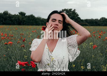 Schöne junge Frau in weißem Kleid, stehend in Mohn Feld Stockfoto