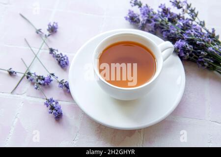 Tasse mit Lavendeltee und frischen Lavendelblüten auf rosa Fliesen Hintergrund Stockfoto