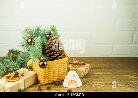 Weihnachtliche festliche Komposition auf einem Holztisch. Korbkorb mit großem Zedernkegel, Fichtenzweigen, Geschenken und einer heißen Kerze Stockfoto