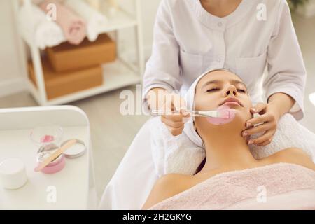 Entspannte junge Frau genießt kosmetische rosa Ton Gesichtsmaske im Beauty-oder Spa-Salon Stockfoto