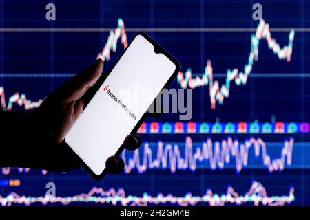 Ein Smartphone mit dem Interactive Broker-Logo in der Hand. Interaktives Aktiendiagramm für Broker im Hintergrund. Stockfoto