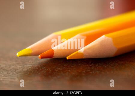 Nahaufnahme der Spitzen von drei Farbstiften in warmen Farbtönen auf einem Holzschreibtisch mit selektivem Fokus. Makrofotografie von gelben und orangefarbenen Bleistiften Stockfoto