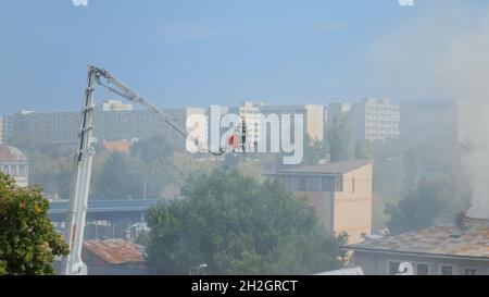 Feuerwehrmänner auf dem Plattformwagen, die auf dem Dach des Hauses in Brand geraten. Ansicht der Feuerwehrleute, die versuchen, das Feuer aus brennendem Gebäude in Flammen und Rauch zu löschen. Männer stoppen Smog und Rauch aus dem Haus. Stockfoto