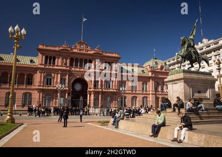 Horizontale Ansicht einiger Menschen, die sich vor dem Eingang der Casa Rosada, Plaza de Mayo, Microcentro, Buenos Aires, Argentinien, ausruhen Stockfoto