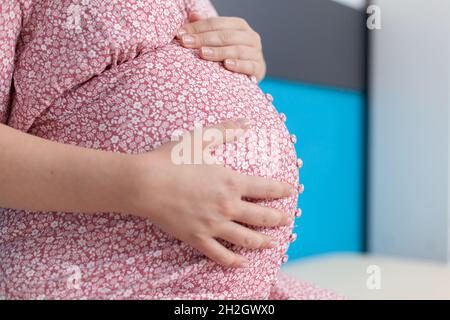 Nahaufnahme einer Schwangeren, die die Hände auf eine Babybumper in der Arztpraxis hält. Patient mit Schwangerschaft erwartet ein Kind und bereitet sich auf die Geburt vor. Person mit Baby im Mutterleib beim Kontrollbesuch Stockfoto