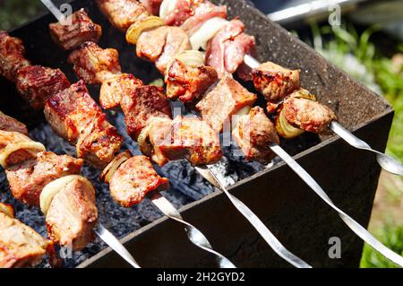 Marinierter Schaschlik, der auf einem Barbecue-Grill über Holzkohle zubereitet wird. Traditioneller russischer Schaschlik auf einem Grillspieß Stockfoto