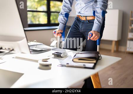 Arbeiter Mit Krücken Am Arbeitsplatz Oder Im Büro. Rehabilitationsleistungen Stockfoto
