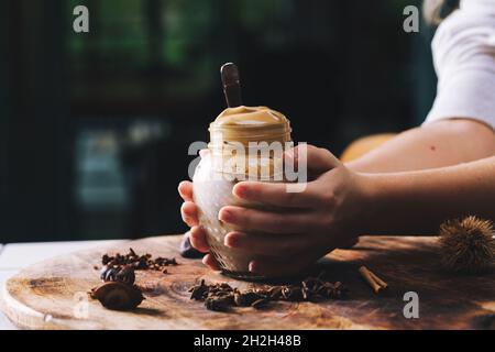 Hausgemachter Dalgona-Kaffee in einem Einmachglas. Hände eines Mädchens, das den Dalgona Kaffee hält. Stockfoto