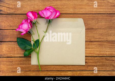 Bouquet von rosa Rosen in einem Umschlag auf einem hölzernen Hintergrund. Postkarte mit Platz für Design. Stockfoto