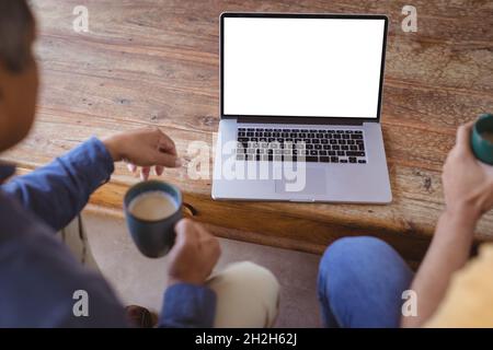 Sohn und älterer Vater mit birazialen Erwachsenen halten Tassen Kaffee und führen einen Videoanruf auf dem Laptop durch Stockfoto