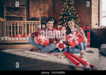 In voller Länge Foto von schönen Mama Papa Tochter Sohn sitzen halten Gegenwart tragen roten Pullover Jeans Socken im Wohnzimmer Stockfoto