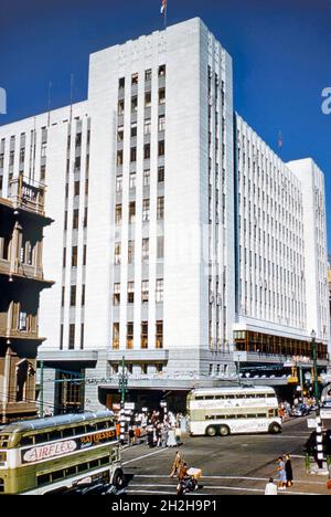 Die Innenstadt von Kapstadt, Südafrika in den 1950er Jahren – Blick auf die Adderley Street mit dem riesigen Kaufhaus OK Bazaars bei strahlendem Sonnenschein. Obusse sind eine der Hauptformen des öffentlichen Verkehrs. Die Straße auf der linken Seite, Castle Street, ist nicht mehr. Es wurde von der Grand Parade und dem Golden Acre Bauprojekt errichtet. Die Adderley Street ist die Hauptstraße des zentralen Geschäftsviertels (CBD) von Kapstadt. Die Trolleybusse auf dem System wurden immer als ‘„spurlose Straßenbahnen“ bezeichnet und die Bushaltestellen wurden als „spurlose Straßenbahnhaltestelle“ markiert – ein altes Foto aus den 1950er Jahren. Stockfoto