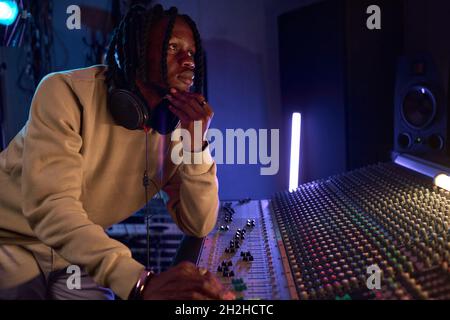 Afrikanischer junger Radio-dj in Kopfhörern mit Musik-Tastatur während der Arbeit am Radio Stockfoto