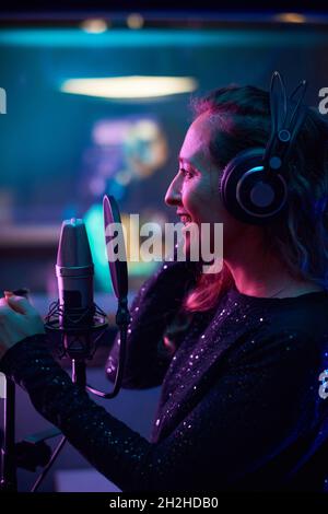 Junge Frau mit Kopfhörern, die im Aufnahmestudio vor dem Mikrofon singt, nimmt ein neues Lied auf Stockfoto