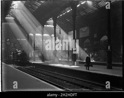 Liverpool Street Station, Liverpool Street, City of London, Greater London Authority, c1932. Ein Blick über das Bahnhofsgebäude an der Liverpool Street Station, der eine Dampfmaschine im Bahnhof zeigt, einen Gepäckträger, der auf einer Plattform Gepäck trägt, und Sonnenstrahlen, die durch das Dach scheinen. Stockfoto