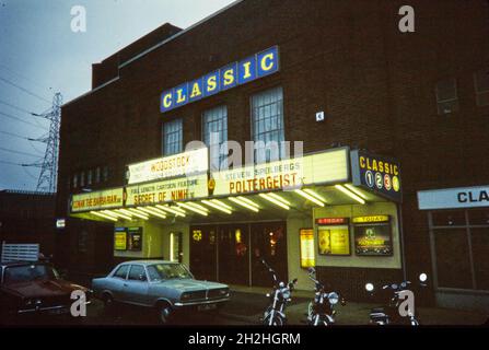 Classic Cinema, Hagley Road West, Quinton, Dudley, 1982. Das Klassikkino, das in der Abenddämmerung von Südosten aus gesehen wird, zeigt das beleuchtete Schild und die Plakatwand mit geparkten Autos und Motorrädern davor. Das Danilo Cinema wurde 1939 eröffnet und war das größte in der Danilo Cinemas-Kette von Mortimer Dent. Es wurde später von Essoldo, Classic, Cannon, ABC, Odeon, Und schließlich von Reel Cinemas. Im frühen 21. Jahrhundert restaurierten Reel Cinemas die Fassade des Gebäudes in ihren ursprünglichen Art-Deco-Stil. Stockfoto