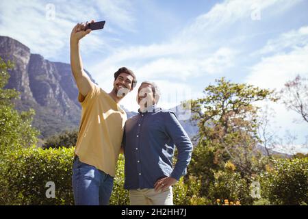 Lächelnder, erwachsener Sohn und älterer Vater, der im Garten ein Selfie mit dem Smartphone gemacht hat Stockfoto