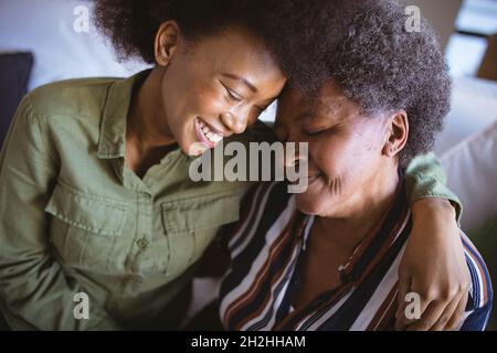Lächelnde afroamerikanische ältere Frau mit ausgewachsener Tochter, die sich mit geschlossenen Augen umarmt Stockfoto