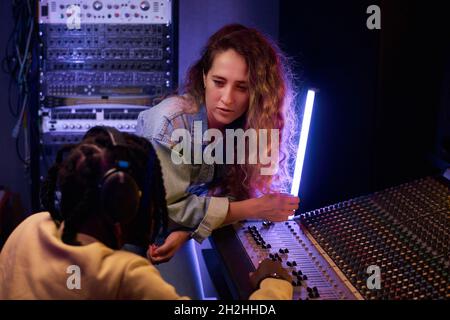 Die junge Sängerin diskutiert mit ihrem Produzenten über neue Songs, während er im Studio am Musikkeyboard arbeitet Stockfoto