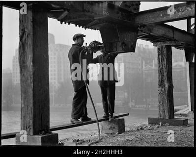 Abriss der Waterloo Bridge, Lambeth, Greater London Authority, 1936. Zwei Männer, die während des Abrisses der alten Waterloo Bridge unter einem Träger arbeiteten. Die Waterloo-Brücke, die während des Abrisses gezeigt wird, wurde von John Rennie entworfen und 1817 eröffnet. Der Abriss der Brücke fand in den 1930er Jahren statt, und die beiden auf dem Foto gezeigten Männer scheinen ein pneumatisches Werkzeug zu verwenden, um einen provisorischen Stahlrahmen zu demontieren, der 1925 errichtet worden war. Die Brücke wurde später in den 1940er Jahren durch eine andere ersetzt. Stockfoto