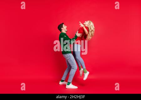 In voller Länge Körpergröße Foto Paar lachen in hässlichen Jumper spielen zusammen isoliert lebendige rote Farbe Hintergrund Stockfoto