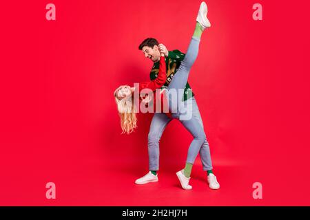 In voller Länge Körpergröße Foto Paar lachen in hässlichen Jumper tanzen zusammen auf Party halten Hände isoliert lebendige rote Farbe Hintergrund Stockfoto