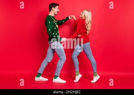 In voller Länge Körpergröße Foto Menschen lachen in hässlichen Jumper tanzen halten Hände isoliert lebendige rote Farbe Hintergrund Stockfoto