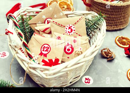 Adventskalender wartet auf Weihnachten. Sammlung von kleinen Umschlägen im Korb mit Zahlen und Aufgaben für Kinder. Saisonale Weihnachtstradition. Stockfoto