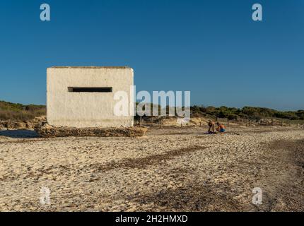 Es Trenc, Spanien; 11 2021. oktober: Alter Bunker des spanischen Bürgerkrieges am Strand von Es Trenc, neben Badegästen, bei Sonnenuntergang. Insel Mallorca, Spanien Stockfoto