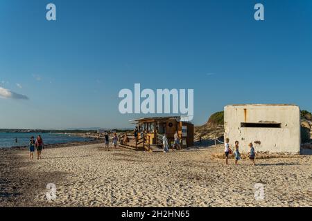 Es Trenc, Spanien; 11 2021. oktober: Alter Bunker des spanischen Bürgerkrieges am Strand von Es Trenc, neben Badegästen, bei Sonnenuntergang. Insel Mallorca, Spanien Stockfoto