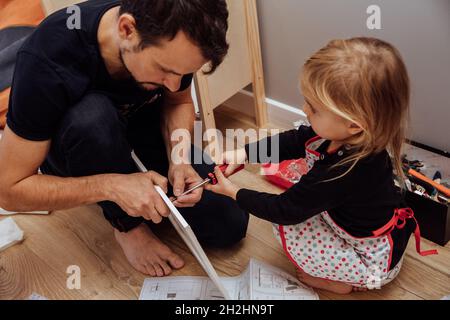 Kleine süße Tochter hilft ihrem Vater, Holzmöbel zu befestigen. Stockfoto