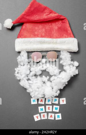 Velvet Santa Hut mit Sonnenbrille Schnurrbart mit Bart und der Aufschrift Happy New Year auf grauem Hintergrund. Neujahrskarte Stockfoto