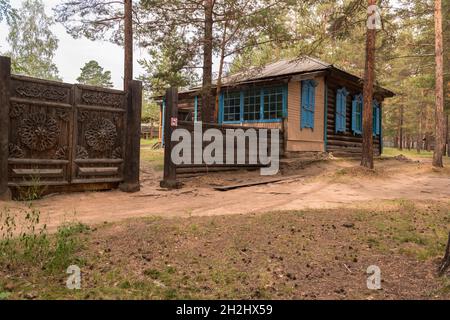 Ein traditionelles Holzhaus mit geschnitztem Zaun zwischen den Bäumen im Ethnographischen Museum in der Nähe von Ulan-Ude. Republik Burjatien, Russland Stockfoto