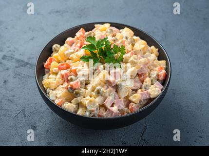 Olivier-Salat in einer schwarzen Schüssel Nahaufnahme auf einem Graphithintergrund. Seitenansicht, horizontal. Stockfoto